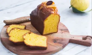 Un delicioso plumcake de limón, recién cortado, con rodajas esponjosas y un limón fresco al fondo.