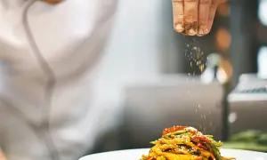 Un chef con título de cocinero espolvorea especias sobre un plato de verduras salteadas.