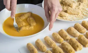 Manos rebozando croquetas en huevo. Se puede congelar la masa de croquetas para freír después.