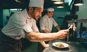 Un chef de partie, con su equipo, supervisa la preparación de un plato en una cocina profesional.
