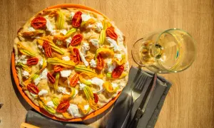 Deliciosa pizza tonda romana con flores de calabacín, tomates secos y ricotta. Un placer para la vista y el paladar.