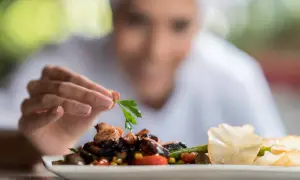 Chef decora plato con perejil, mostrando sus habilidades de un cocinero. Pulpo, verduras y chips de patata.