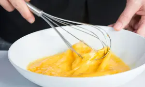 Manos batiendo huevos en un bol blanco, un paso clave para que es emulsionar y lograr texturas perfectas en la cocina.