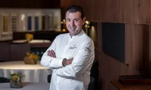 Chef sonriente en su cocina, con el logo de Ricard Camarena Restaurantes en su uniforme.