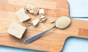 Bloques de levadura fresca y una cuchara con levadura seca granulada sobre una tabla de cortar. Se puede congelar la levadura fresca para conservarla.