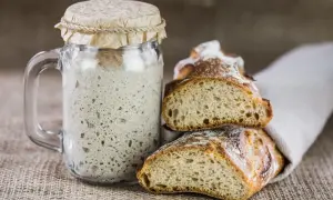 Masa madre burbujeante en un frasco junto a pan recién horneado. La clave para un buen pan está en el tiempo y temperatura para hornear pan.