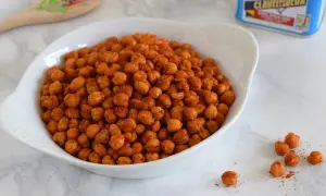 Un tazón blanco lleno de garbanzos fritos crujientes, sazonados con especias rojizas.