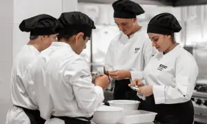 Estudiantes en cursos de cocina para profesionales, concentrados en sus tareas en una cocina profesional.