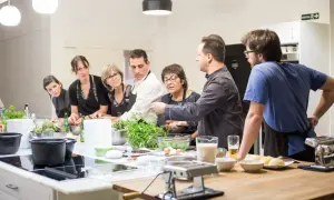 Grupo de personas aprendiendo en un curso de cocina mediterránea. Ingredientes frescos y utensilios listos para cocinar.