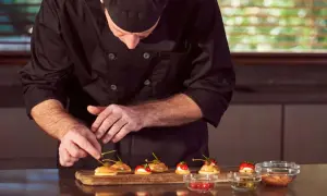 Chef en uniforme negro prepara canapés con salmón y alcaparras. Cada detalle cuenta en este arte de metre de cocina.