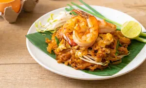 Pad Thai con camarones, perfecto para tu curso de cocina tailandesa. Servido sobre hoja de plátano, con brotes de soja, cebolleta y limón.