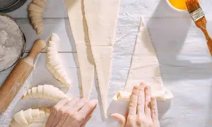 Manos enrollando masa para croissants. ¡Se pueden congelar los croissants para hornearlos más tarde!