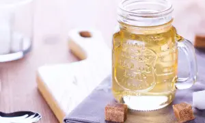 Jar de vidrio con líquido dorado, ideal para tu azucar invertida receta. Cubos de azúcar y tabla de madera al fondo.