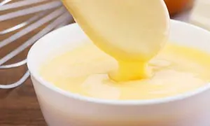 Crema pastelera cremosa cayendo de una cuchara a un bol. ¡Es bueno saber que se puede congelar la crema pastelera para usarla más tarde!