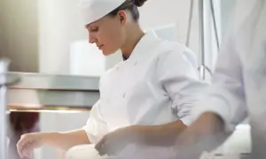Chef concentrada en su labor, junto a otro chef en la cocina.