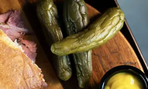 Un sándwich de pastrami como se come, con pepinillos y mostaza.