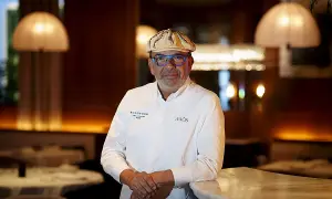 Un chef español con estrella Michelin, con gafas azules y gorra, posa en un elegante restaurante.