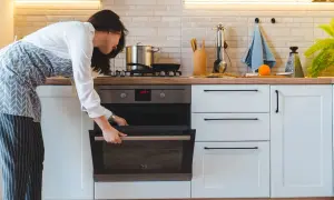 Mujer abre horno para cocinar al vapor en horno convencional.
