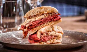 Mollete de pastrami con abundante carne curada y salsa cremosa, apilado en un plato oscuro.