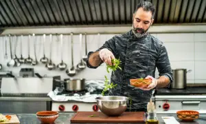 Chef con barba añade hierbas a un bol. Su trabajo en la direccion de cocina FP es impecable.