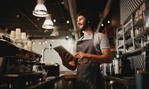 Gerente de un restaurante revisa pedidos en su tableta, sonriendo.