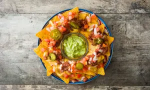 Nachos con queso derretido, carne, tomate, cebolla y jalapeños, con guacamole en el centro.