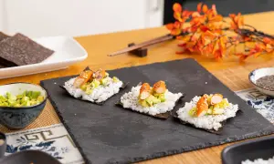 Tres pequeños rollos de sushi en proceso, listos para aprender a hacer sushi. Arroz, aguacate y palitos de cangrejo sobre alga nori.