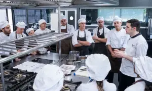 Estudiantes en un curso gestión restaurantes gratis, atentos a las instrucciones de un chef en una cocina profesional.