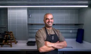 Chef sonriente con delantal negro en una cocina moderna, uno de los cocineros vascos famosos.