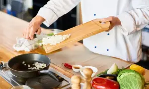 Un jefe de cocina, con su blanco uniforme, prepara cebolla picada para una sartén. Un convenio de sabor se inicia.