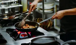 Manos expertas cocinan en sartenes sobre fuego vivo, un arte que se aprende en las mejores escuelas de cocina en España.