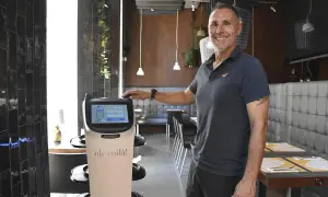Un hombre sonriente junto a un robot que sirve comida en un restaurante moderno.
