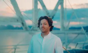 Jean Imbert, con camisa blanca, posa frente a una estructura de barco al atardecer.