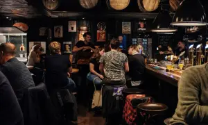 Gente en un bar oscuro, con barriles en el techo. Se preguntan cuanto gana un bar al mes mientras beben cerveza.