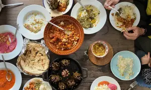 Mesa llena de platos variados, perfectos para recetas de cenas con amigos. Hummus, garbanzos, alcachofas y pan pita.