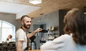 Barista sonríe mientras prepara café, un paso más para abrir su restaurante.