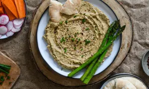 Hummus cremoso con espárragos, pan de pita y crudités de zanahoria y rábano. ¡Perfecto para tus ideas de picoteo saludables!