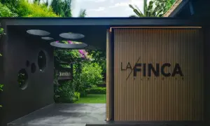 Entrada a "La Finca" de Susi Díaz, un jardín exuberante con un letrero de madera y una fachada moderna.