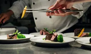 Chef emplata un plato de carne con brócoli y zanahoria, un detalle digno de una estrella verde Michelin.