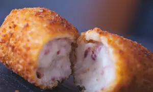 Croqueta dorada y crujiente, partida por la mitad, revelando un interior cremoso. La proporción de harina y leche para croquetas es clave para esta textura.