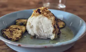 Rape a baja temperatura, jugoso y tierno, servido con rodajas de calabacín a la parrilla en un plato azul.