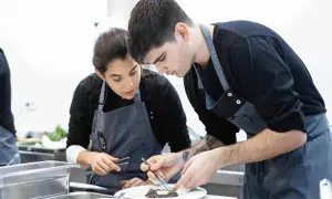 Dos aprendices de cocina, concentrados en emplatar un plato, aprendiendo como ser chef.