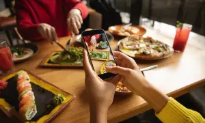 Persona toma foto de su comida en un restaurante para compartir en redes sociales. Se ven sushi, pizza y ensalada.