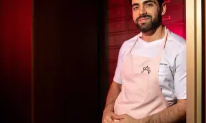 Chef Serrano, parte de la lista cocineros estrellas Michelin, sonríe con delantal rosa.