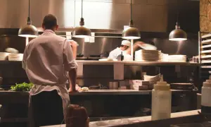 Un ayudante de cocina en España prepara ingredientes frescos en una cocina profesional, con pilas de platos y utensilios listos para el servicio.