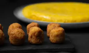 Croquetas doradas y crujientes, un ejemplo de que es la quinta gama hostelería, con una tortilla española al fondo.