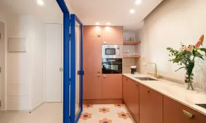 Cocina moderna con armarios naranjas, encimera de mármol y suelo hexagonal. Perfecta para un curso intensivo de cocina.