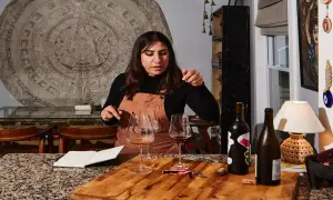 Mujer explicando cómo ser sommelier, con copas de vino y botellas en una mesa.