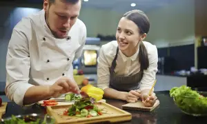 Chef instructor muestra cómo emplatar una ensalada a una alumna atenta en cursos de chef.