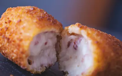 Croqueta dorada y crujiente, partida por la mitad, revelando un interior cremoso. La proporción de harina y leche para croquetas es clave para esta textura.